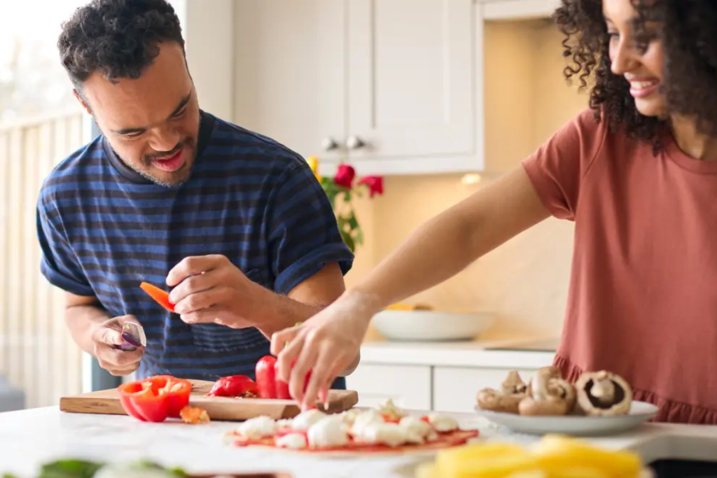 Disabled man cutting vegetables in the kitchen with his carer